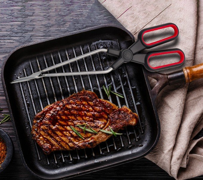 Viper tongs resting in a cast-iron grill pan beside a seared steak